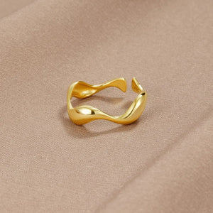 Goldener wellenförmiger Ring, offenes Design, liegend auf beigem Stoff | Fashion Peak