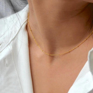 Feine goldene Kugelkette am Hals einer Frau mit weißem Hemd getragen | Fashion Peak