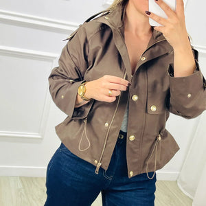 Braune kurze Trenchcoat-Jacke mit Kordelzug, getragen von blonder Frau, Jeans | Fashion Peak