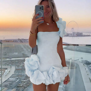 Weißes One-Shoulder-Minikleid mit Blütenapplikation, getragen von blonder Frau auf Balkon | Fashion Peak