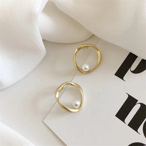 Goldene ovale Ohrringe mit Perle, flach liegend auf weißem Stoff | Fashion Peak