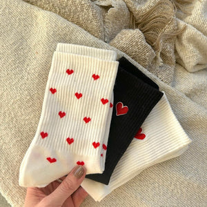 Hand hält drei gefaltete Socken mit roten Herzen, weiß und schwarz | Fashion Peak