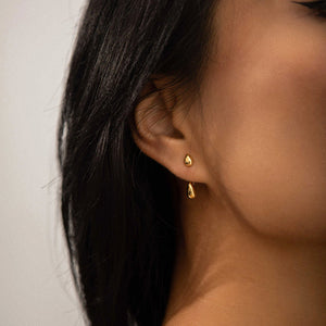 Goldener tropfenförmiger Ohrstecker am Ohr einer dunkelhaarigen Frau getragen | Fashion Peak