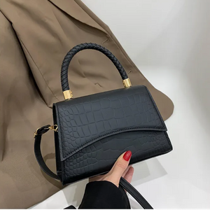 Schwarze Handtasche mit Kroko-Prägung und geflochtenem Griff, von Hand gehalten | Fashion Peak
