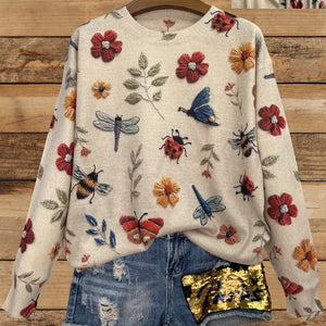 Beiger Strickpullover mit Blumen-, Schmetterlings- und Marienkäfermuster, auf Kleiderbügel hängend | Fashion Peak