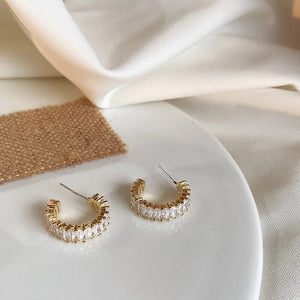 Goldfarbene Creolen mit Zirkonia besetzt, freigestellt auf weißem Teller liegend | Fashion Peak
