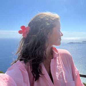 Frau mit lockigem Haar trägt pinke Blumen-Haarklammer vor Meerblick | Fashion Peak