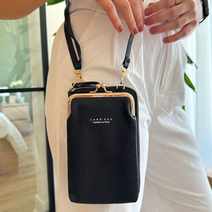 Schwarze Umhängetasche mit goldenen Details, getragen von einer Person in Weiß | Fashion Peak