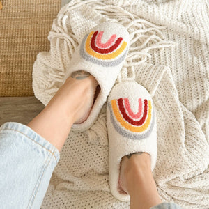 Beige Plüsch-Hausschuhe mit buntem Regenbogenmuster, getragen an zwei Füßen | Fashion Peak