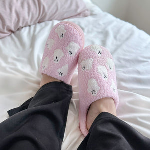 Rosa Plüsch-Hausschuhe mit Geistermuster, getragen an Füßen auf Bett | Fashion Peak