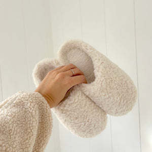 Cremeweiße Teddy-Plüsch Hausschuhe werden von einer Hand hochgehalten | Fashion Peak