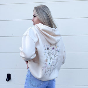 Cremefarbener Oversized-Hoodie mit Blumenstickerei, getragen von blonder Frau vor Wand | Fashion Peak
