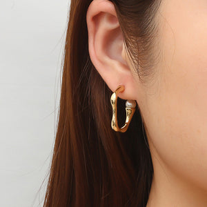 Getragener goldener Creolen-Ohrring mit Wellenform am Ohr einer Frau | Fashion Peak