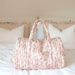 Gesteppte Reisetasche rosa Blumenmuster mit Henkeln, stehend auf weißem Bett | Fashion Peak