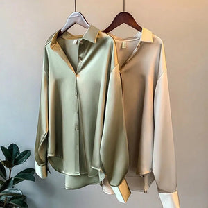 Zwei satinierte Hemdblusen in Salbeigrün und Beige hängen auf Kleiderbügeln | Fashion Peak