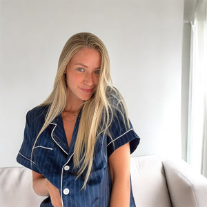 Frau trägt dunkelblauen gestreiften Satin-Schlafanzug mit weißer Paspel, sitzend | Fashion Peak