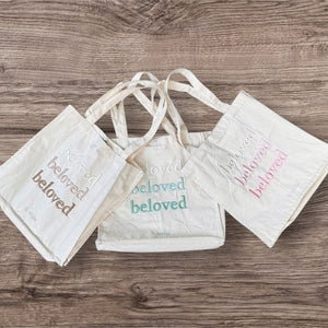 Drei beige Canvas-Taschen mit Stickschrift, flach liegend auf Holzuntergrund | Fashion Peak