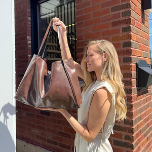 Frau hält braune glänzende Kunstleder Shopper Tasche vor Backsteinwand hoch | Fashion Peak