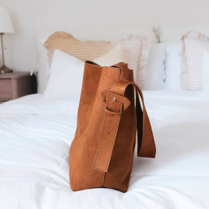 Braune Schultertasche in Wildleder-Optik steht aufrecht auf weißem Bett | Fashion Peak