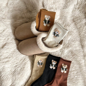 Fünf Paar Socken mit Bärenstickerei, flach neben beigen Hausschuhen liegend | Fashion Peak